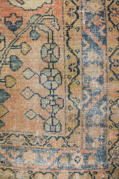 Close-up of an antique rug's handwoven, detailed pattern in muted peach and navy tones.
