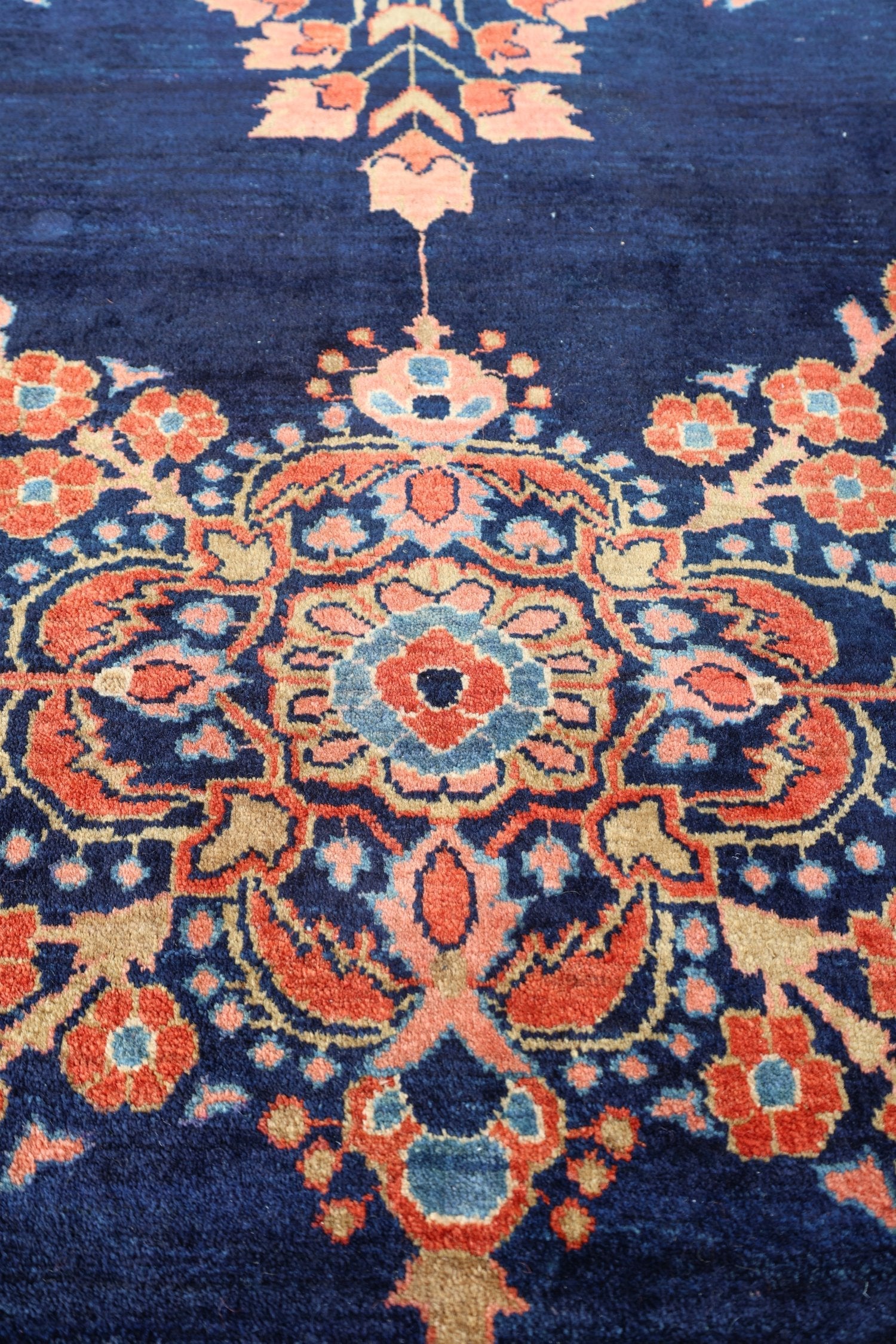 Close-up of a navy blue antique rug with intricate floral patterns in shades of red, orange, and beige.
