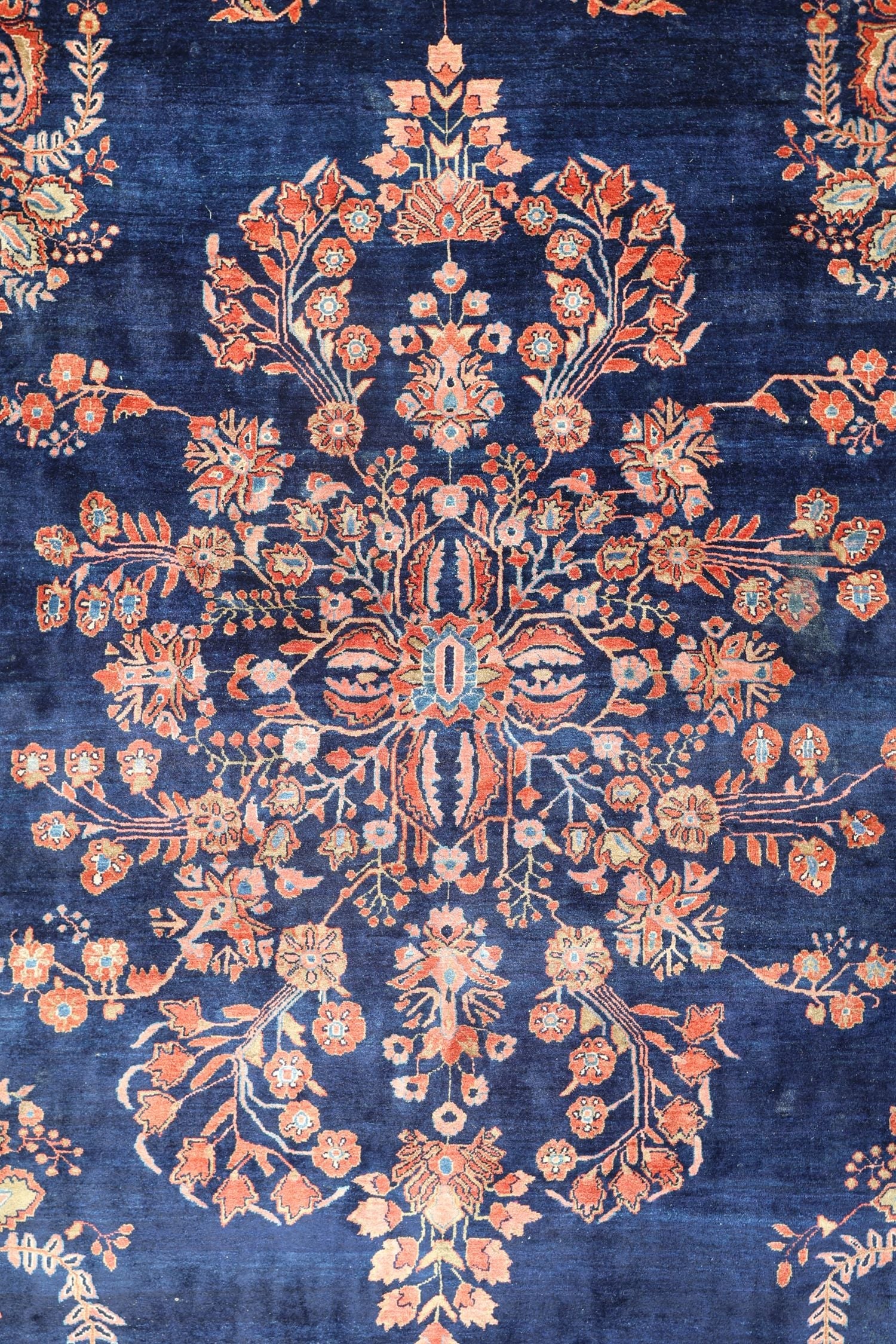 Detail of antique rug, navy blue background with intricate coral floral pattern, handwoven.
