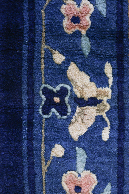 Close-up of a deep blue antique rug's handwoven floral pattern.
