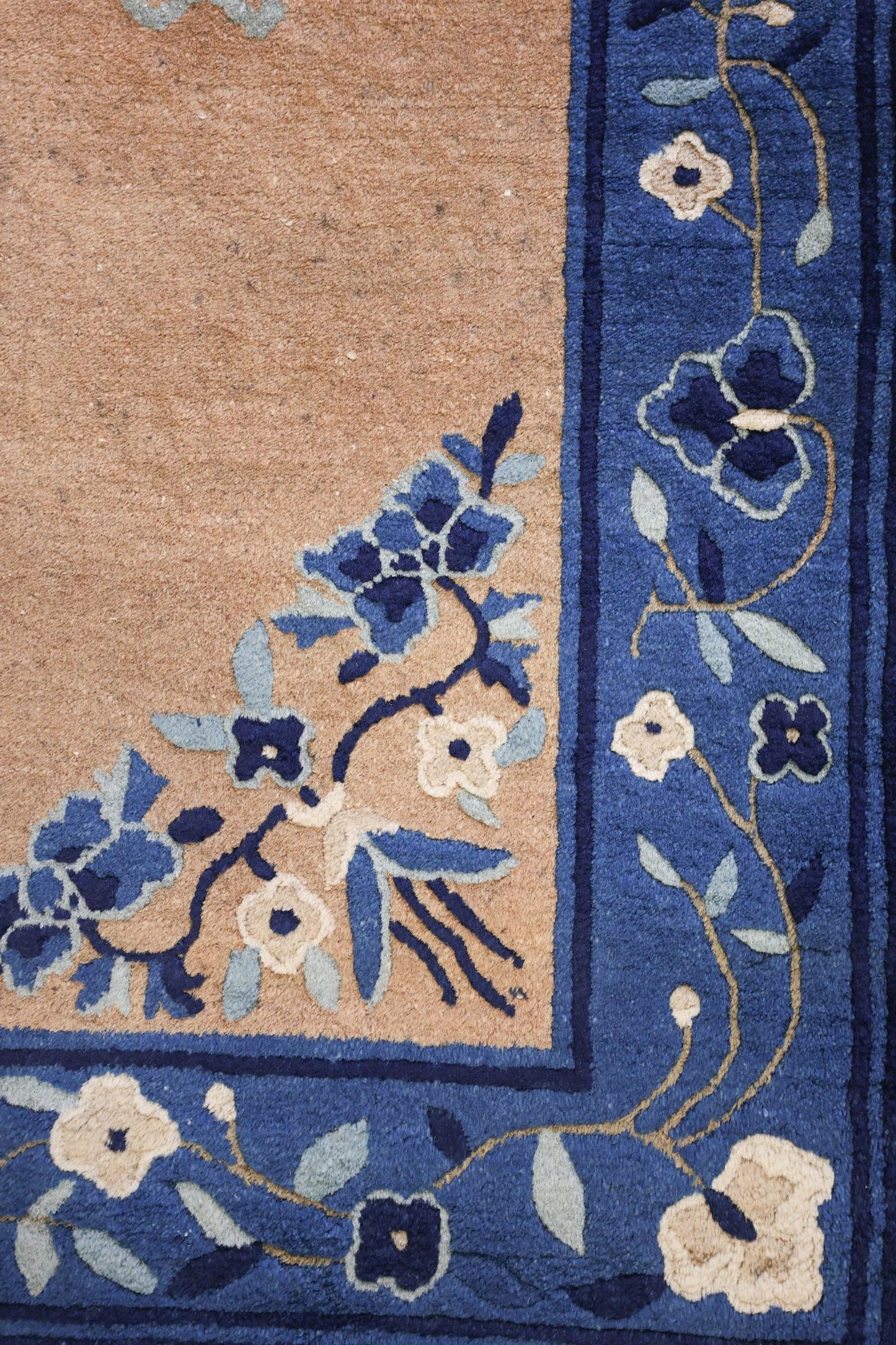 Close-up of antique rug's blue floral border, detailed handwoven design on beige background.
