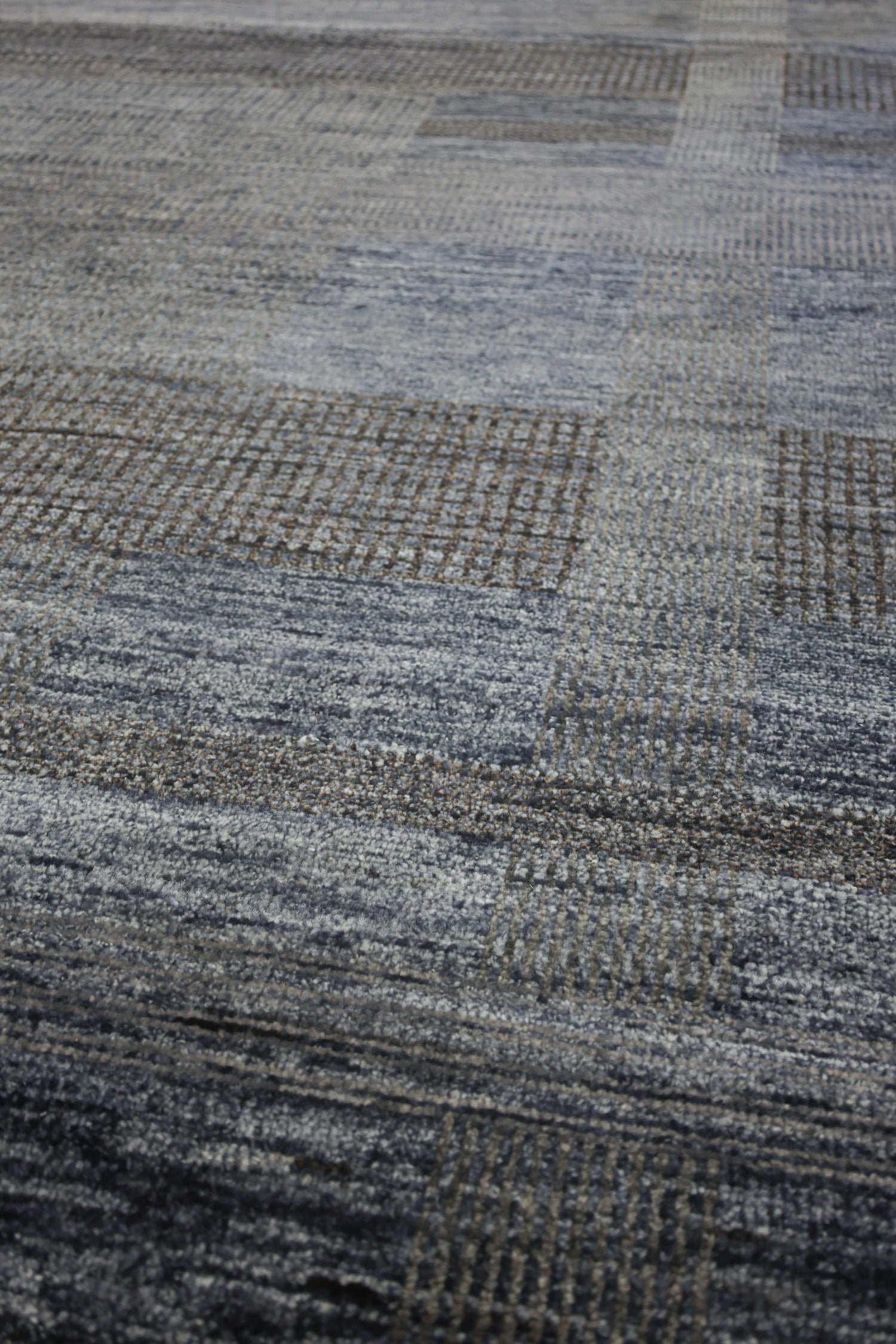 Handwoven rug detail: textured grey and brown plaid pattern, close-up view.
