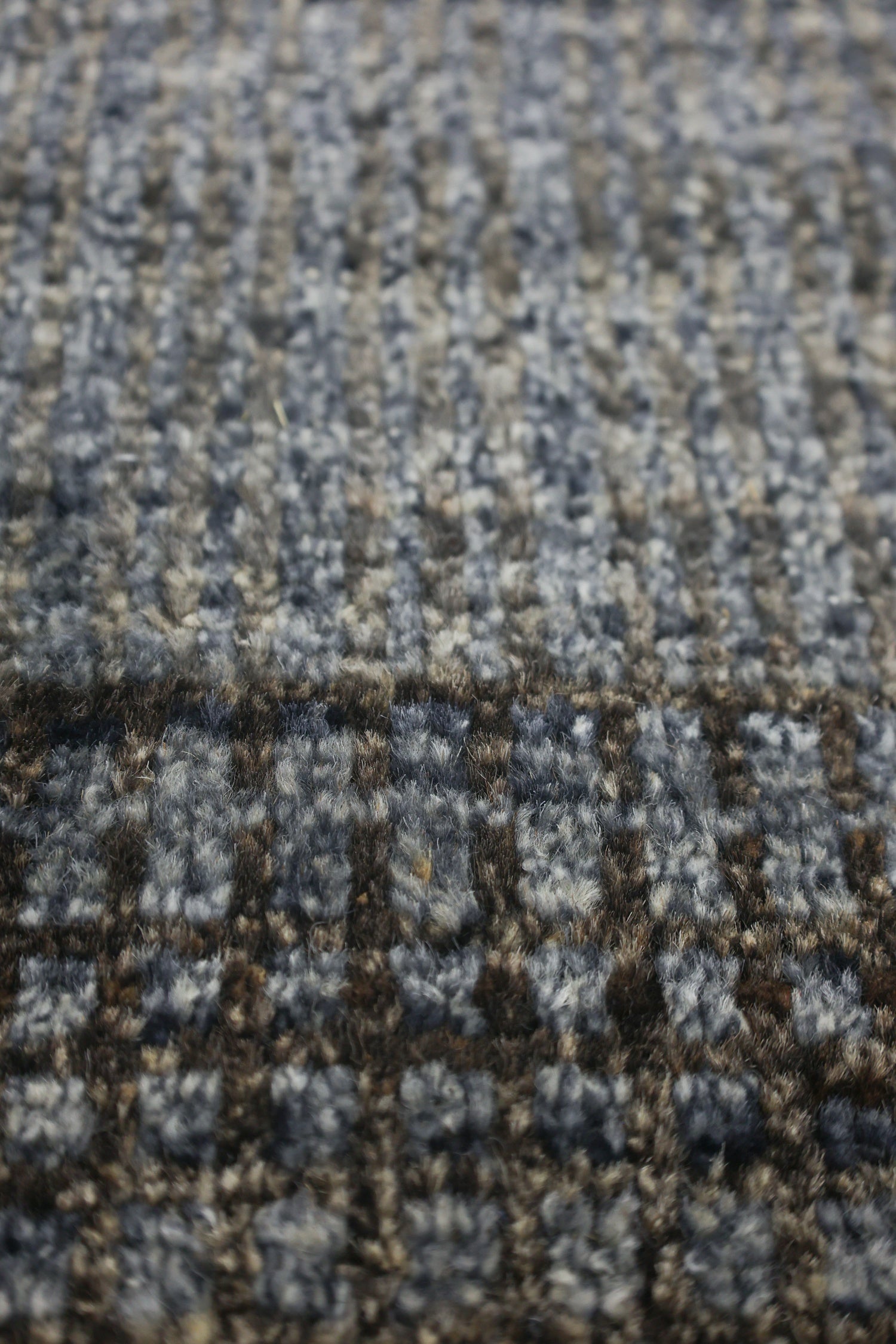 Close-up of a textured rug with an abstract plaid pattern in shades of gray and brown.
