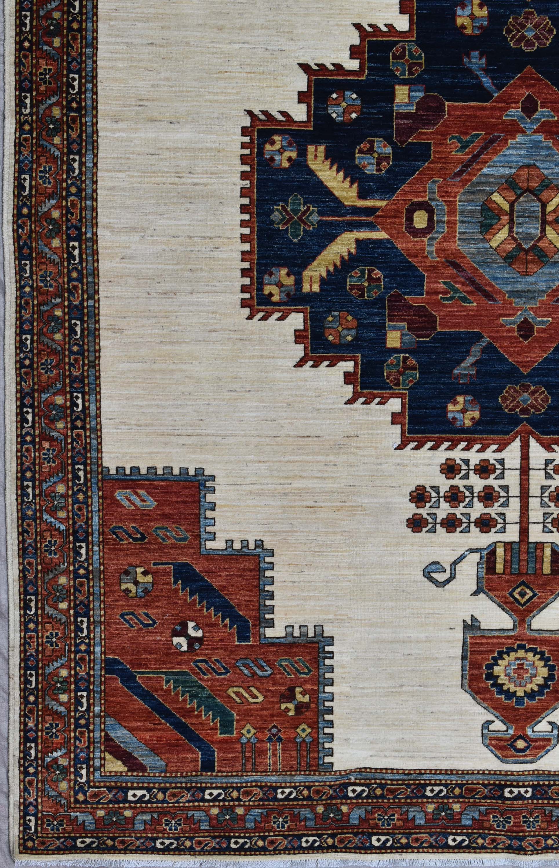 Handwoven rug detail: intricate border, cream field, and navy, red, and gold tribal pattern.
