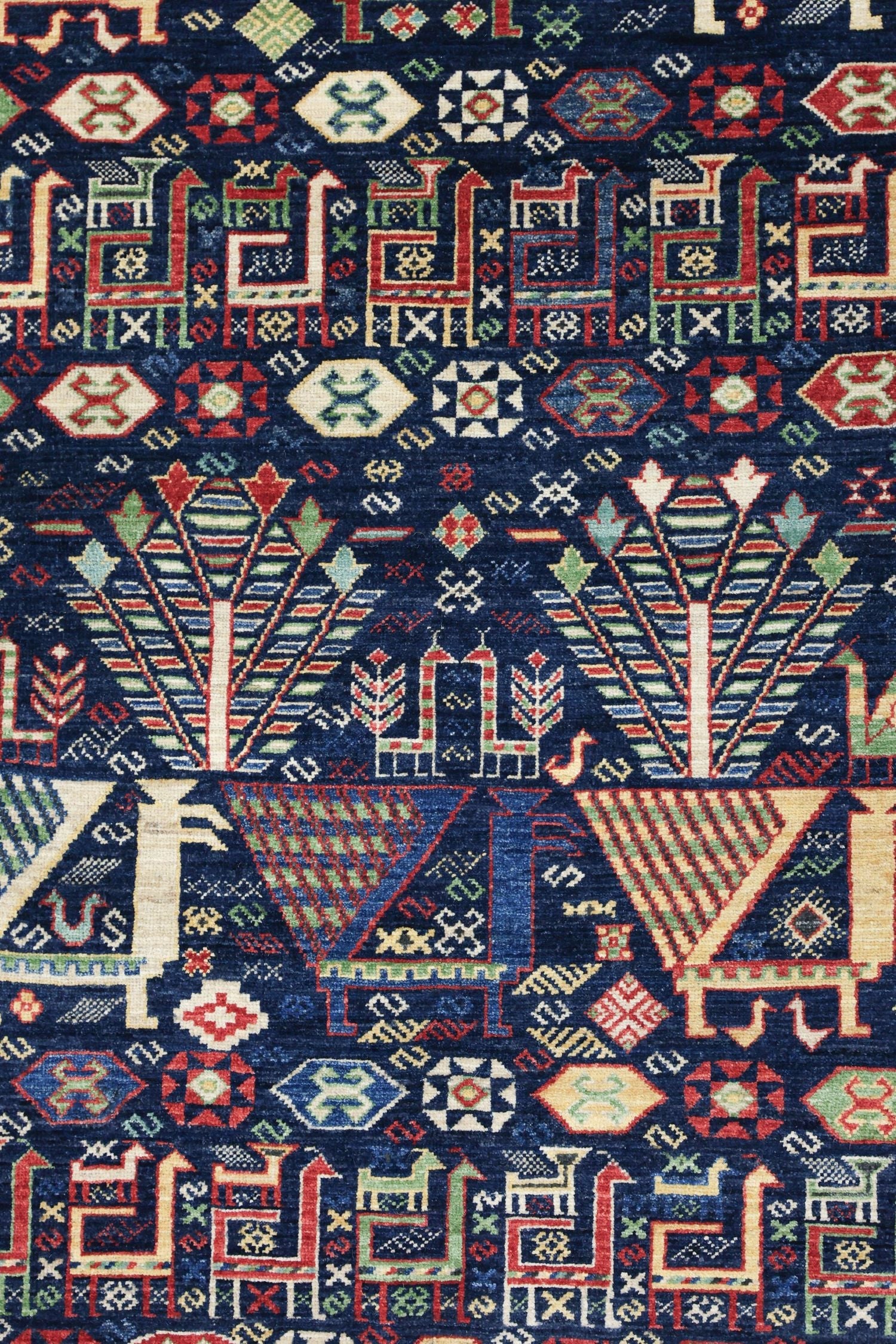 Handwoven rug detail: vibrant tribal pattern in navy, red, green, and cream; intricate geometric and stylized animal motifs.

