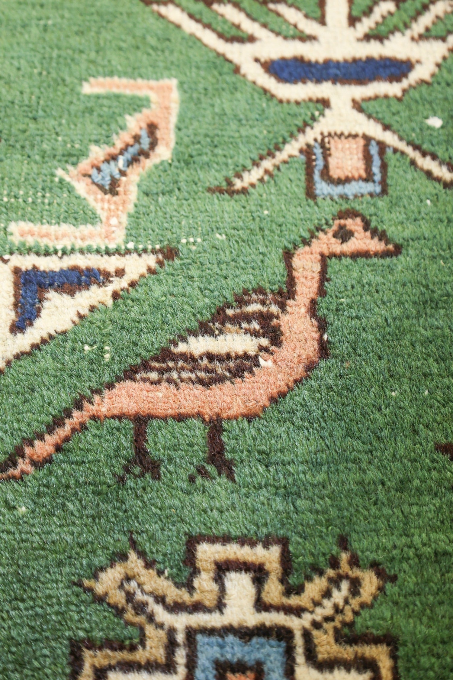 Close-up of antique rug detail: hand-woven, green field with bird motif, earthy tones.

