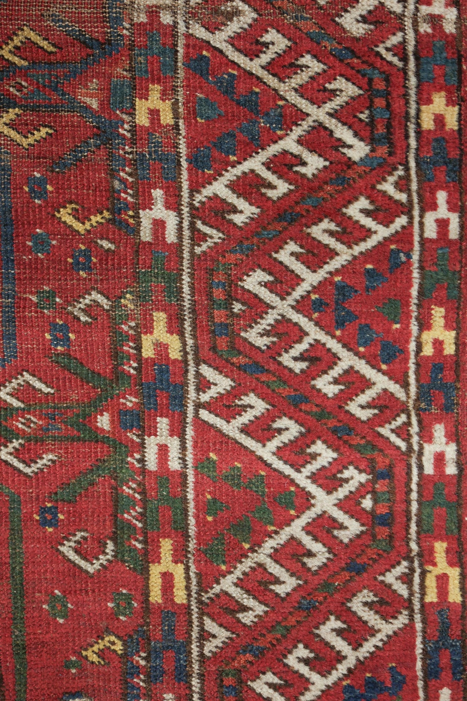 Close-up of antique rug detail; red, white, and blue geometric patterns in handwoven textile.
