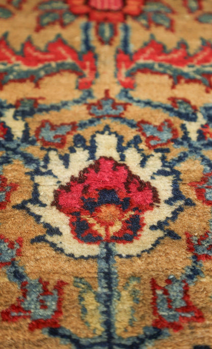 Close-up detail of an antique rug's handwoven floral pattern in red, blue, and beige.
