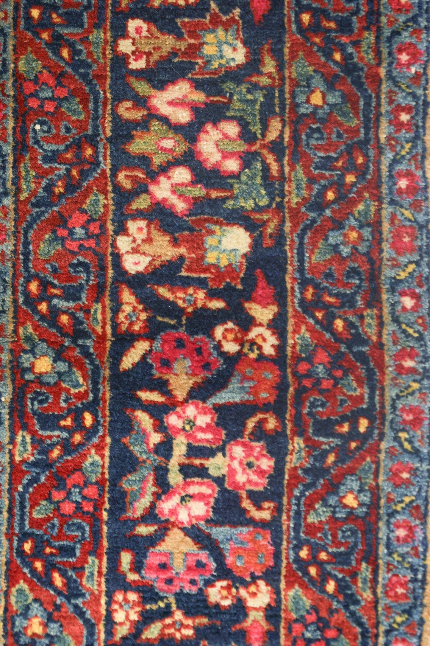 Close-up of antique Bijar rug's detailed floral pattern in rich reds, blues, and creams.
