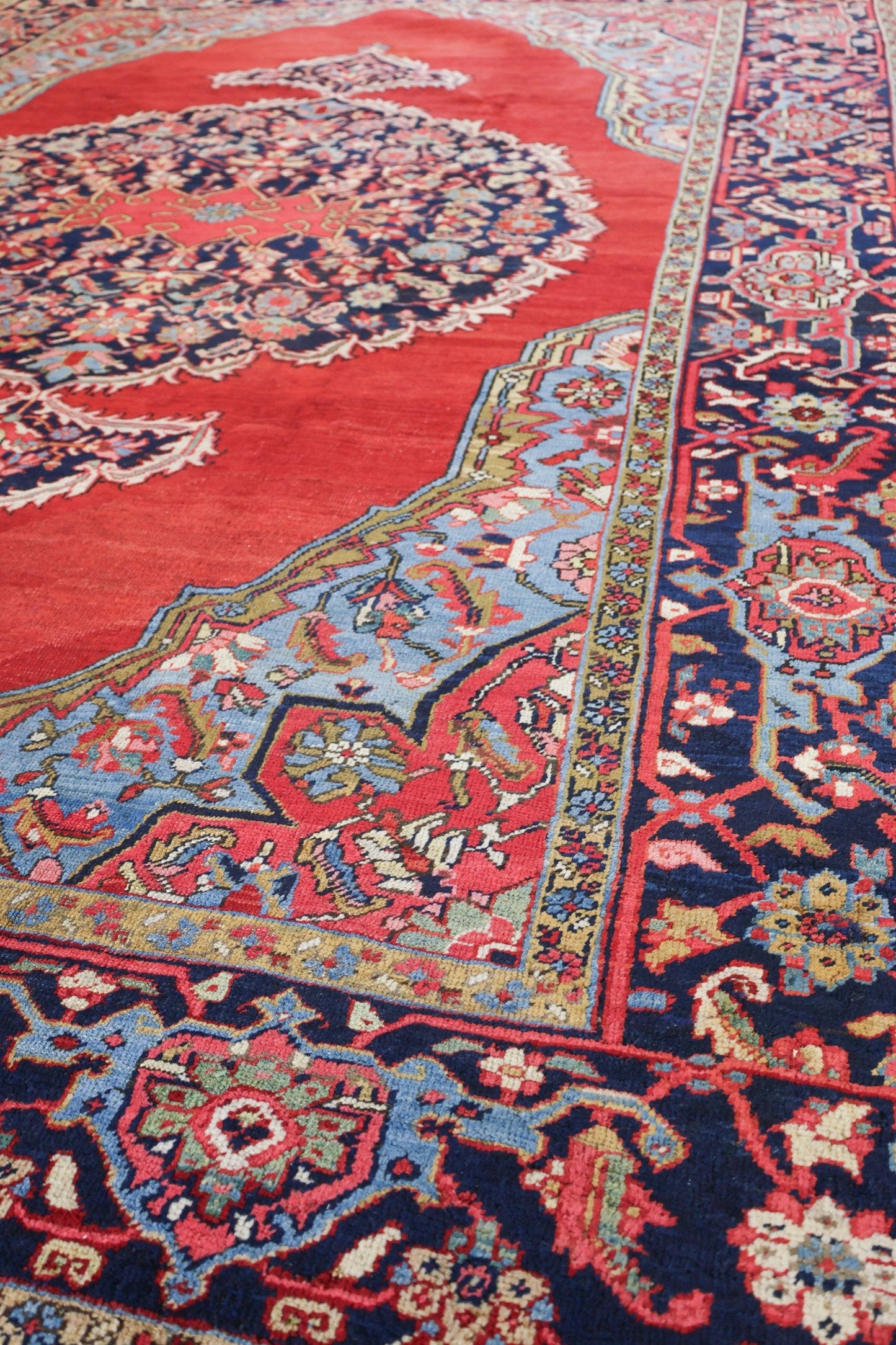 Handwoven Heriz rug detail: red, blue, and ivory floral pattern on a dark navy border.
