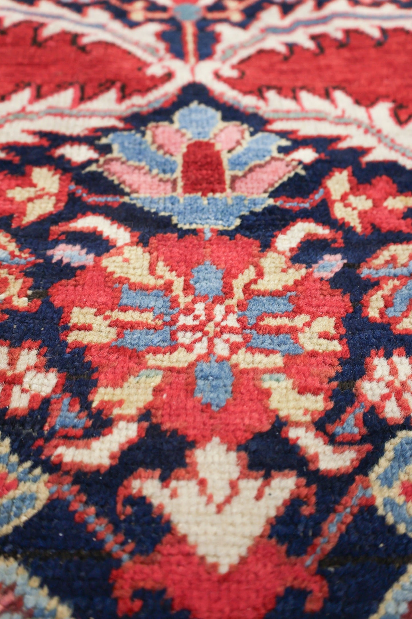 Close-up of a handwoven rug's detailed floral pattern in red, blue, and cream.
