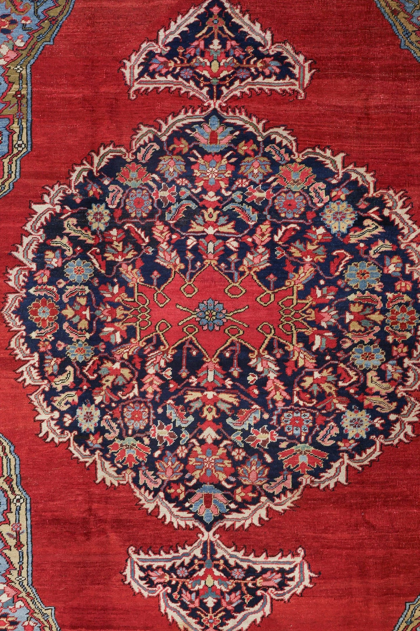 Handwoven rug detail: intricate floral medallion in navy, red, and cream on a rich red background.

