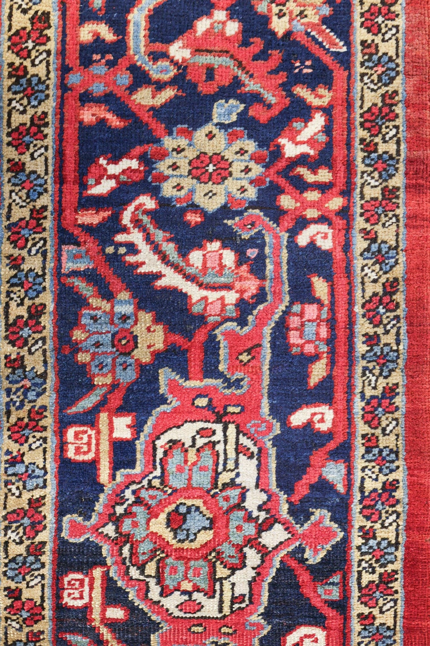Handwoven Heriz rug detail: rich red, blue, and beige floral pattern, antique tribal design.
