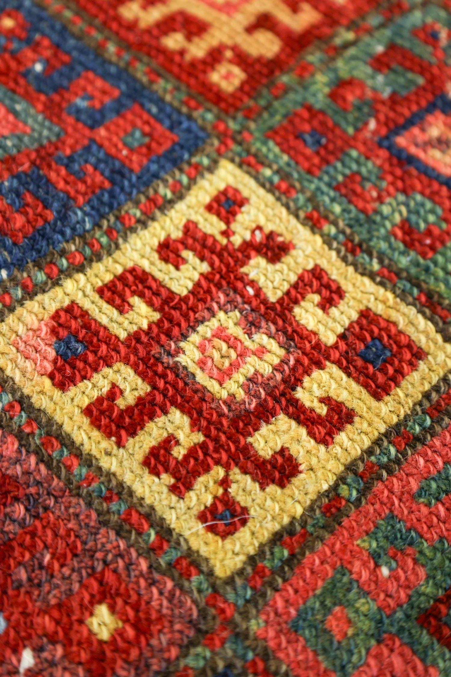Close-up of antique handwoven rug detail, showcasing vibrant red, gold, and blue geometric patterns.
