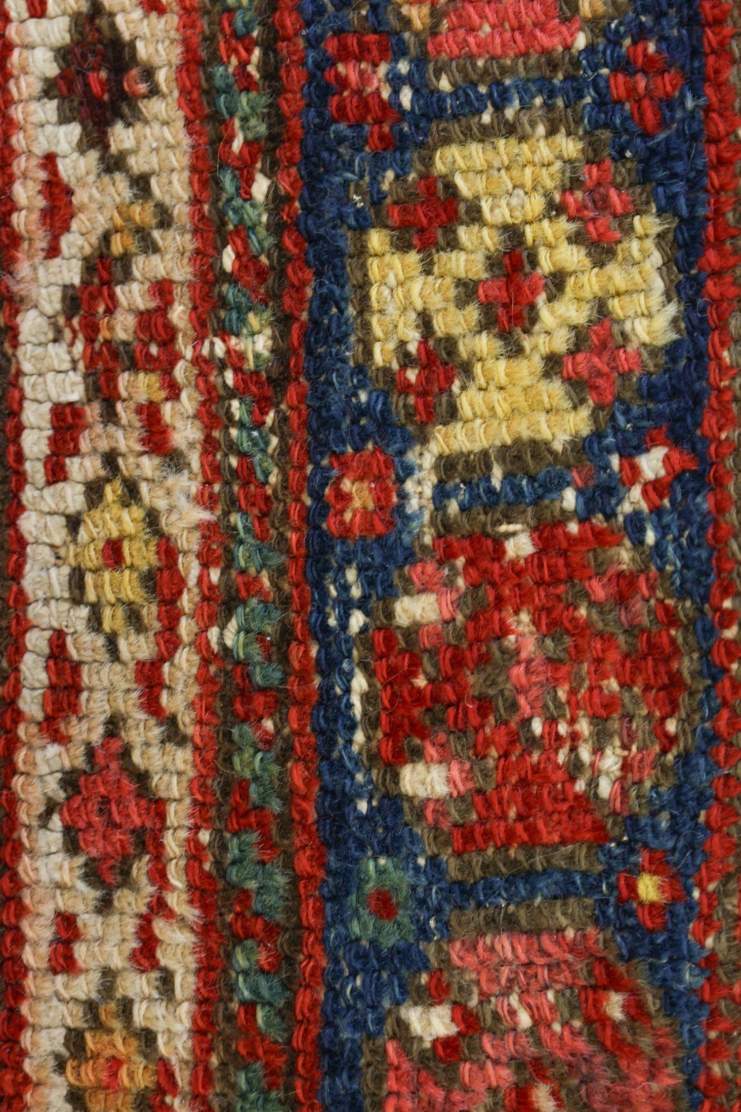 Close-up view of antique rug's detailed handwoven texture, showcasing red, beige, and blue wool threads.
