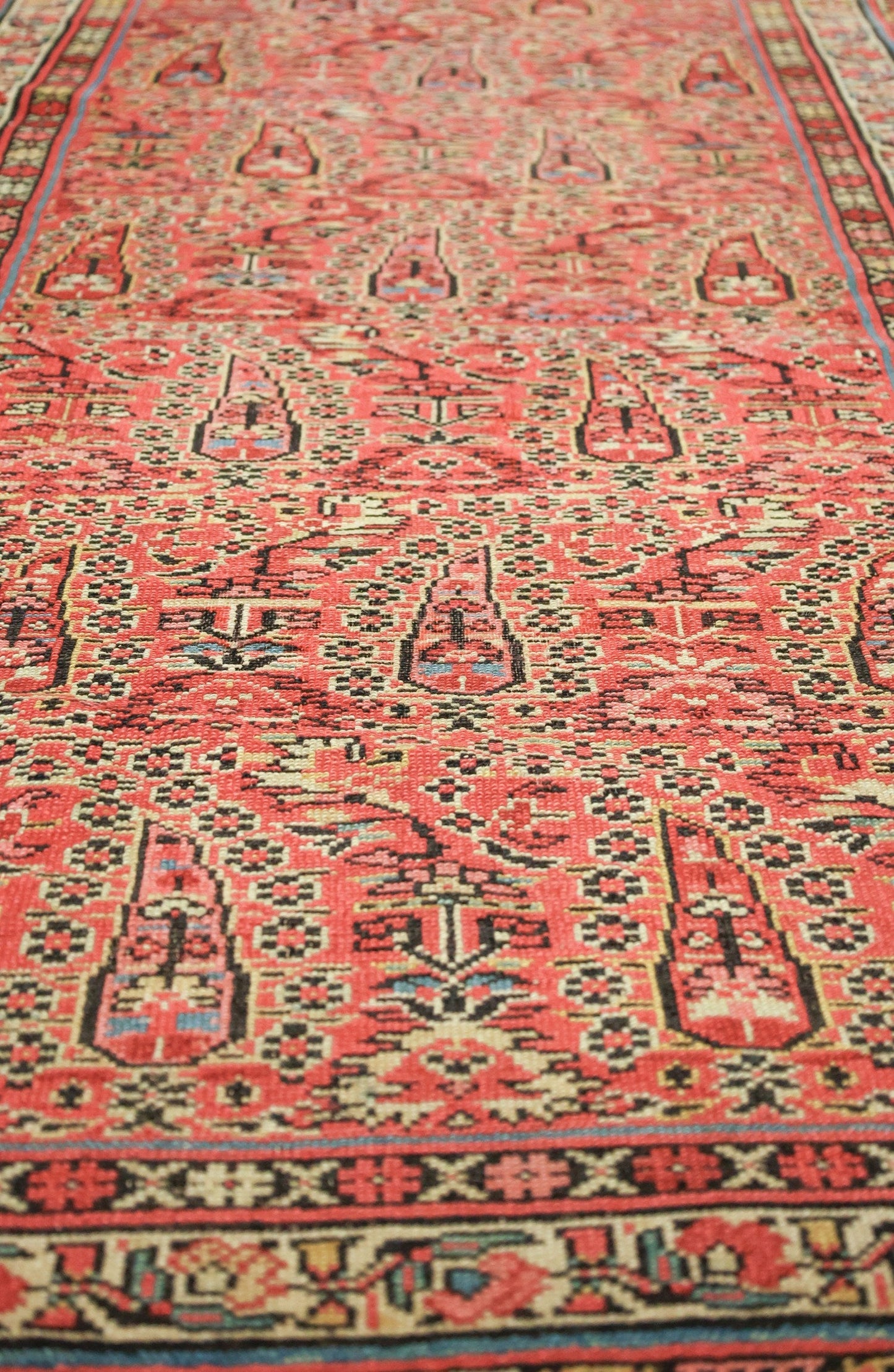 Intricate detail of a handwoven antique Persian rug, predominantly red with black and muted color accents.
