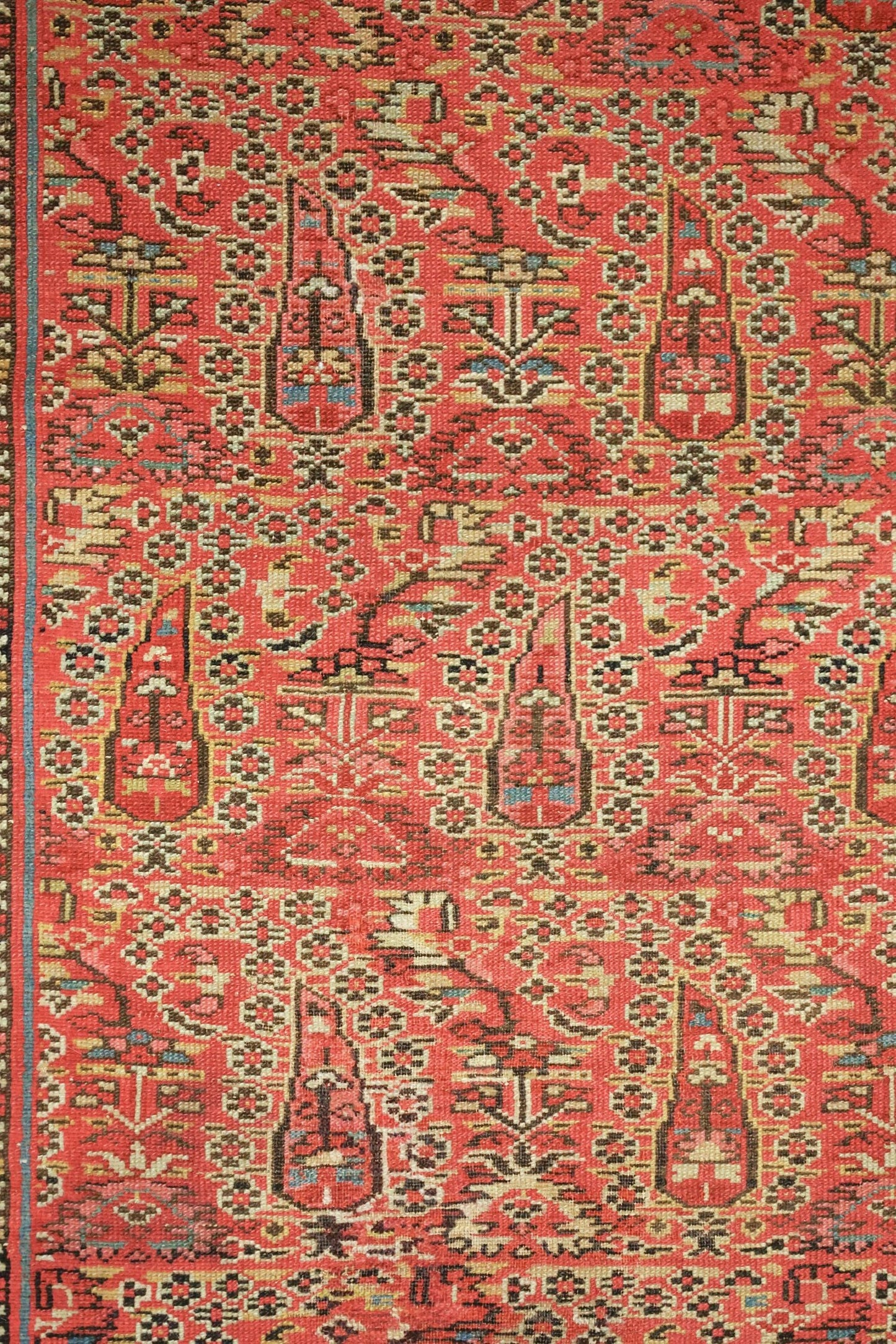 Intricate detail of an antique Persian rug, showcasing a red and brown handwoven pattern.
