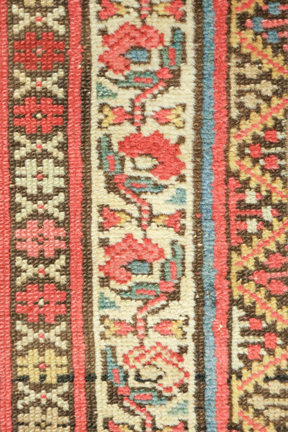 Close-up detail of antique Persian rug, showcasing handwoven floral pattern in red, beige, and teal.
