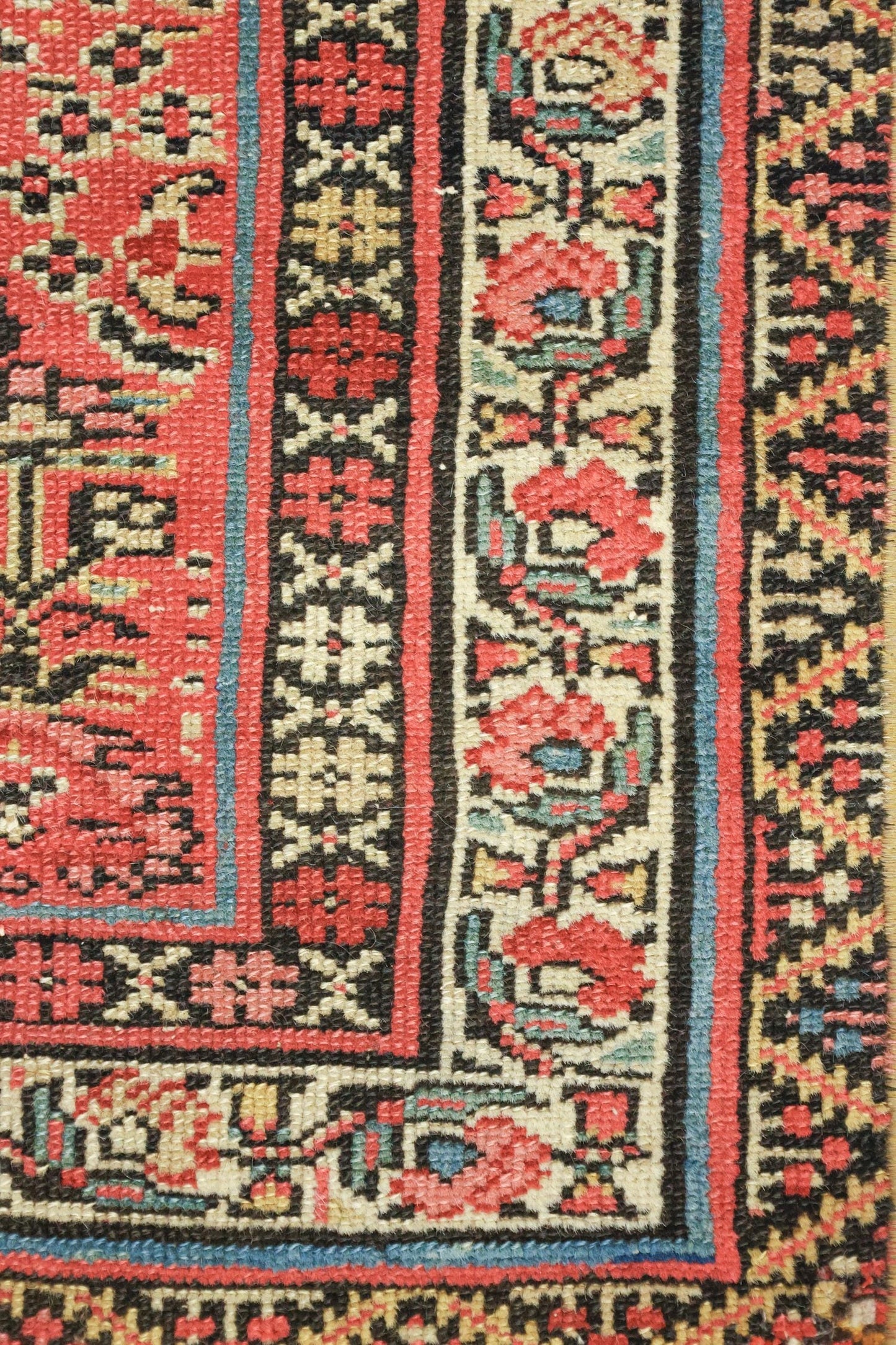 Close-up detail of antique rug's handwoven border, showcasing red, black, and cream floral patterns.

