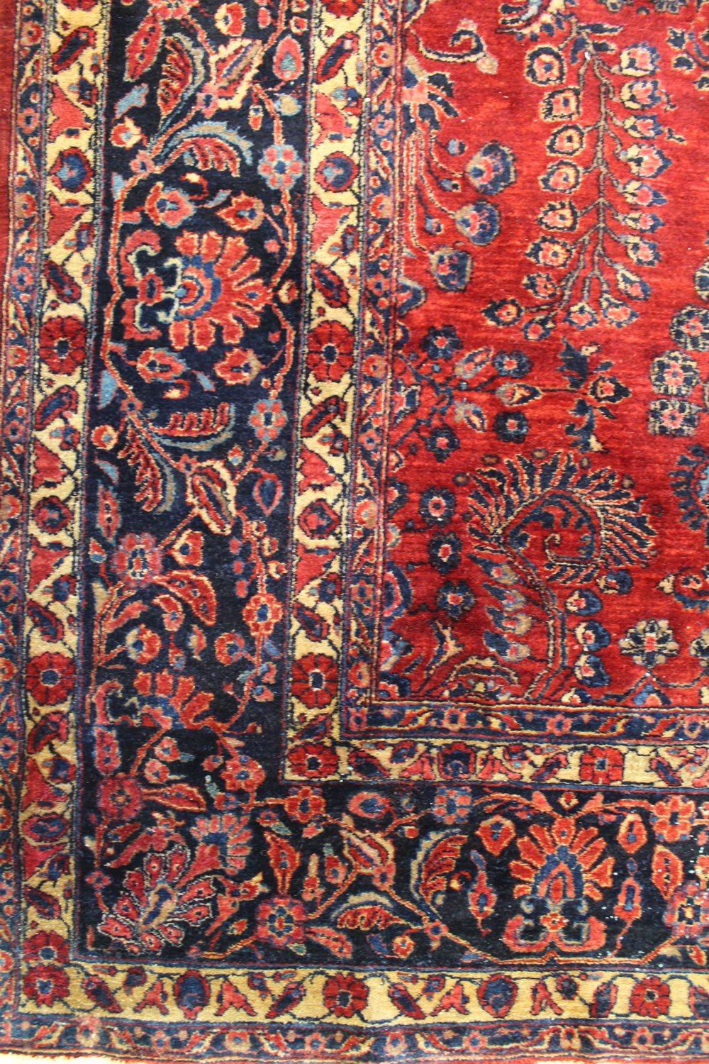 Detail of antique rug's handwoven floral pattern in red, blue, and beige.
