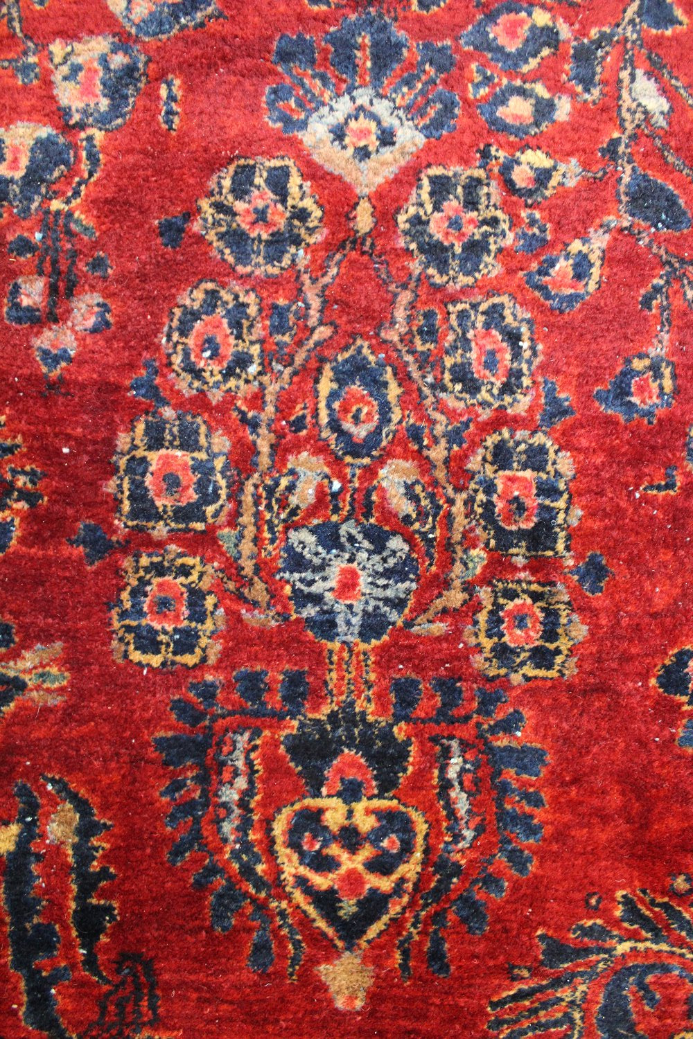 Close-up of a richly colored antique rug with intricate floral details in navy and gold on a red background.
