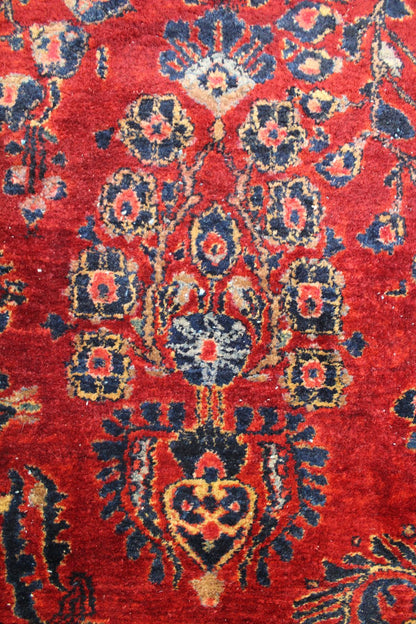 Close-up of a richly colored antique rug with intricate floral details in navy and gold on a red background.
