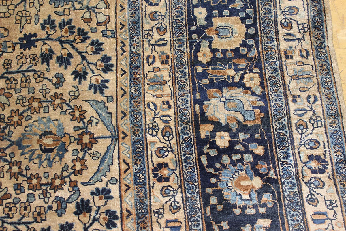 Detail of antique Mashad rug's intricate blue and beige floral pattern.
