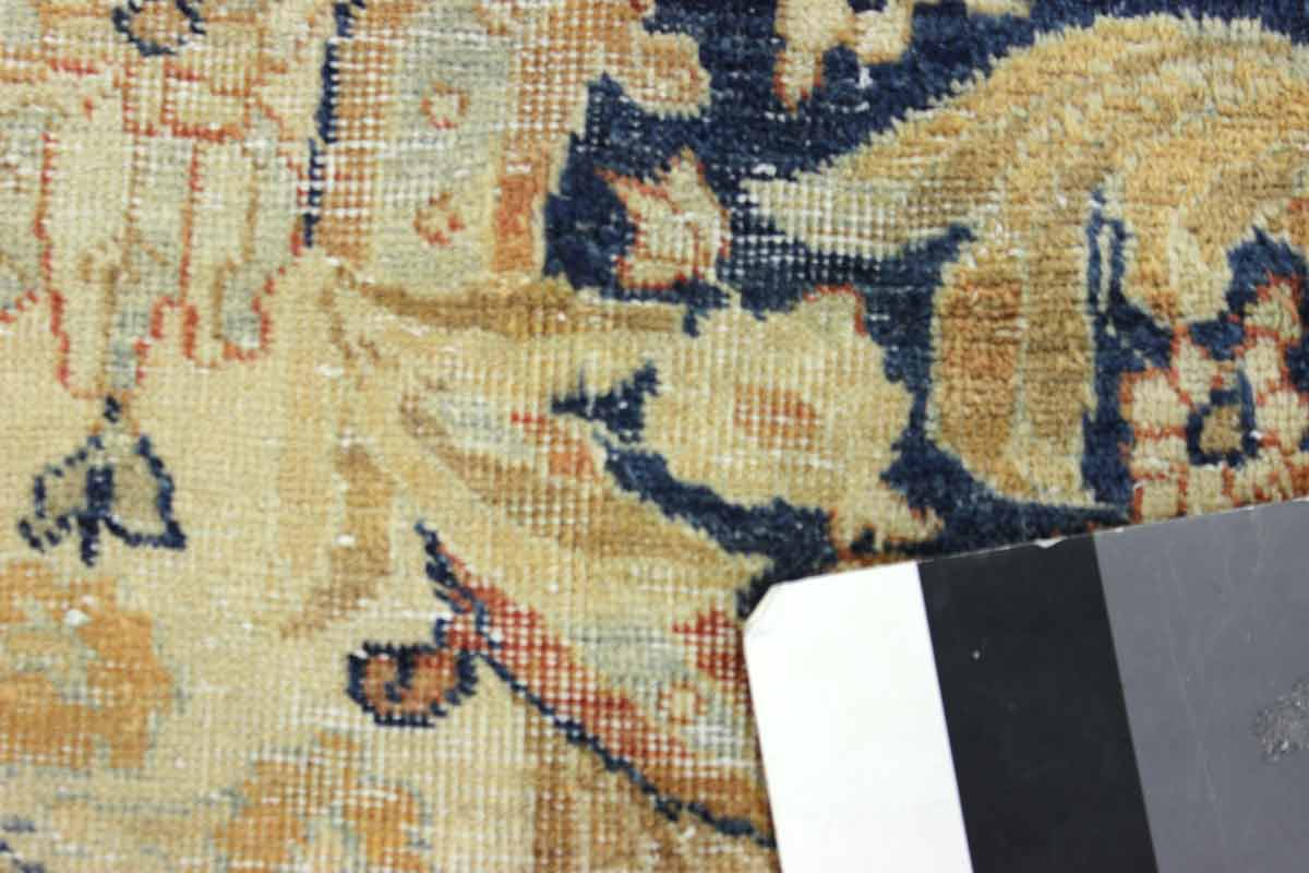 Close-up of antique rug detail, showcasing handwoven floral pattern in beige and navy.
