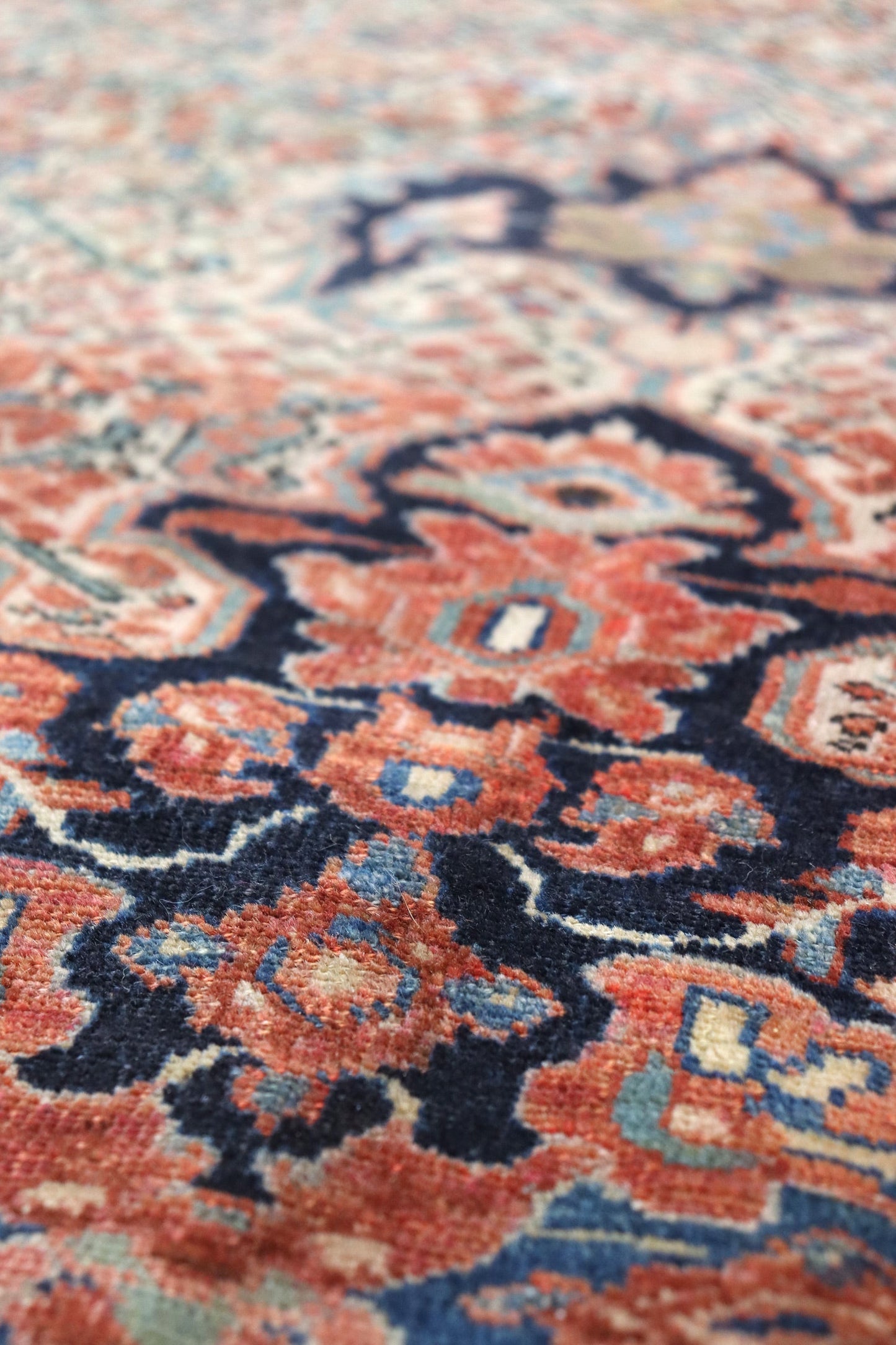 Close-up detail of a handwoven rug, showcasing intricate red, blue, and ivory patterns.
