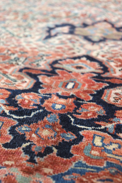 Close-up detail of a handwoven rug, showcasing intricate red, blue, and ivory patterns.
