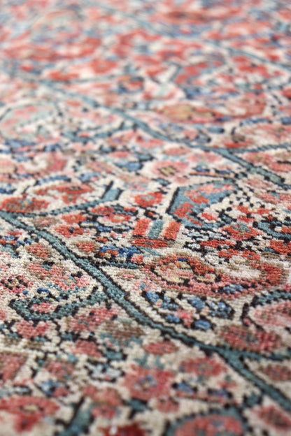 Close-up of antique rug's intricate, handwoven design in muted reds, blues, and creams.
