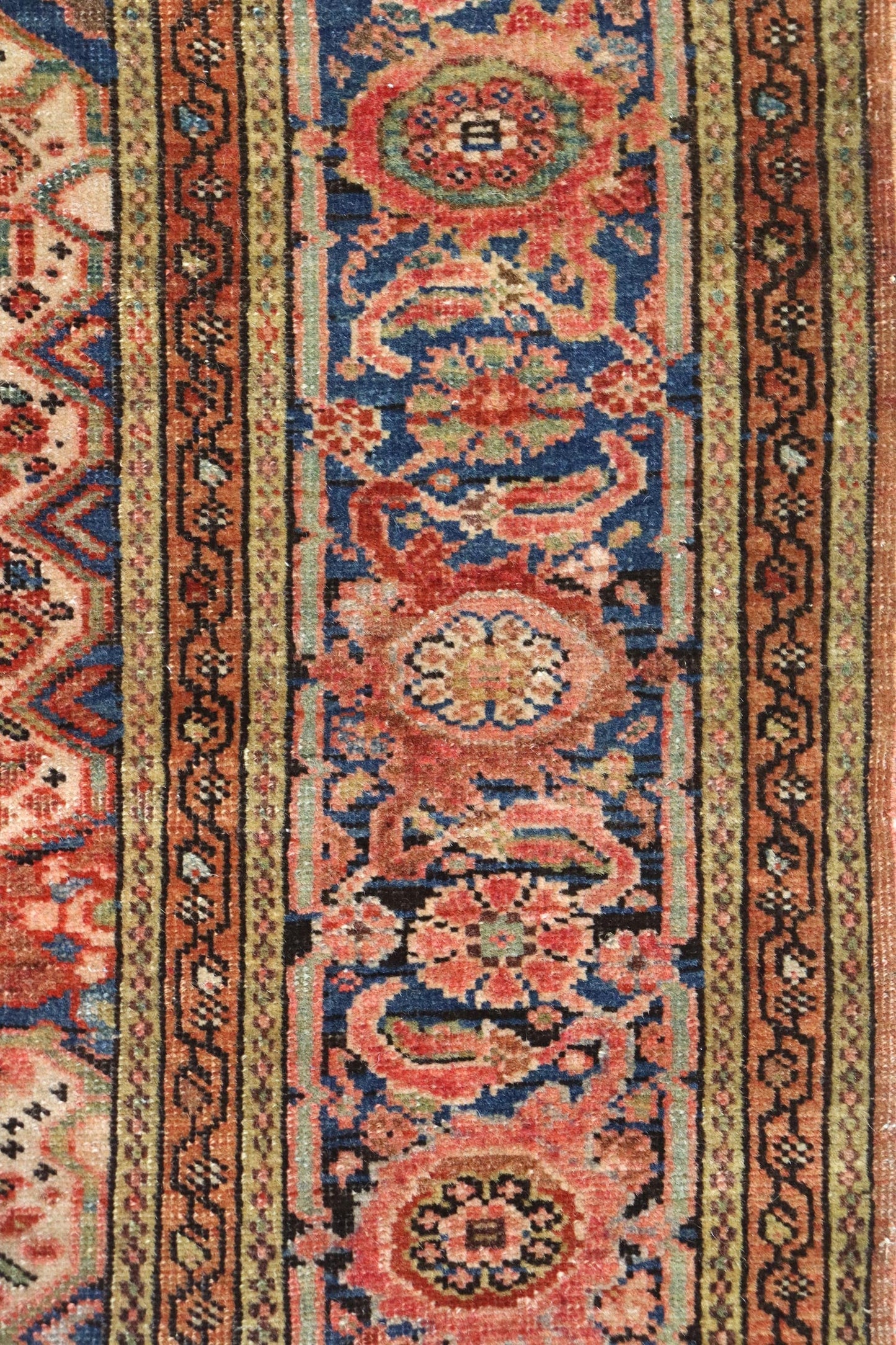Close-up of antique rug detail, showcasing handwoven floral pattern in reds, blues, and beige.
