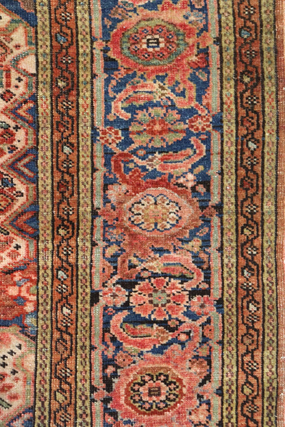 Close-up of antique rug detail, showcasing handwoven floral pattern in reds, blues, and beige.
