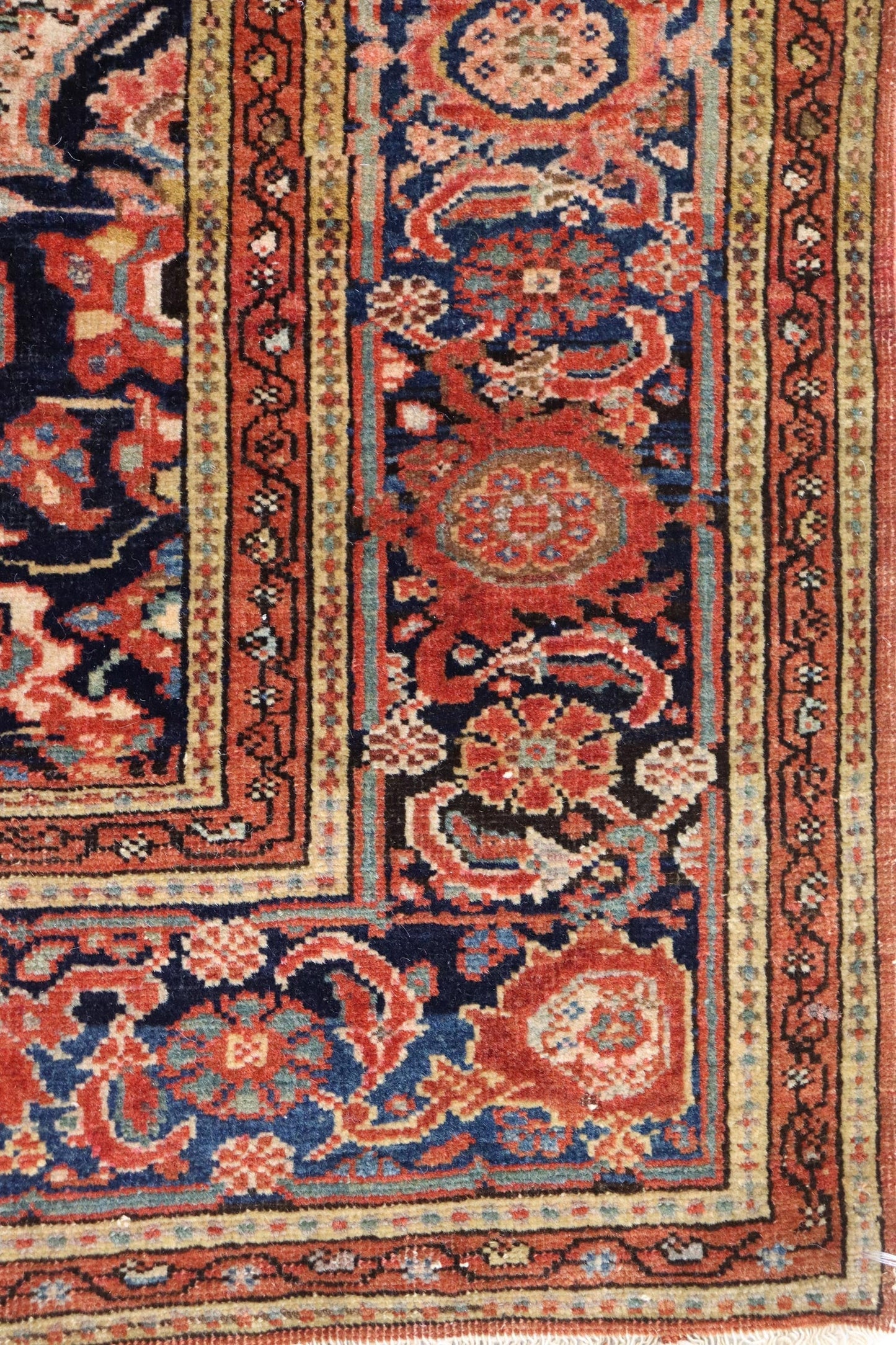 Handwoven rug detail: rich red, blue, and beige floral pattern, antique Ferahan Sarouk style.
