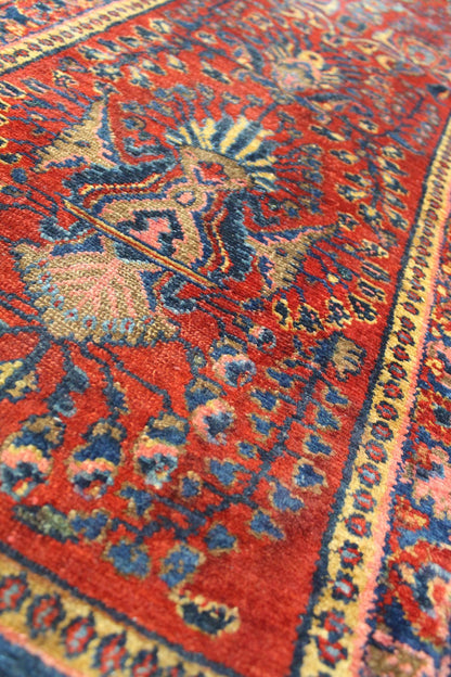 Close-up of antique handwoven rug, showcasing rich red tones and intricate blue and gold floral patterns.

