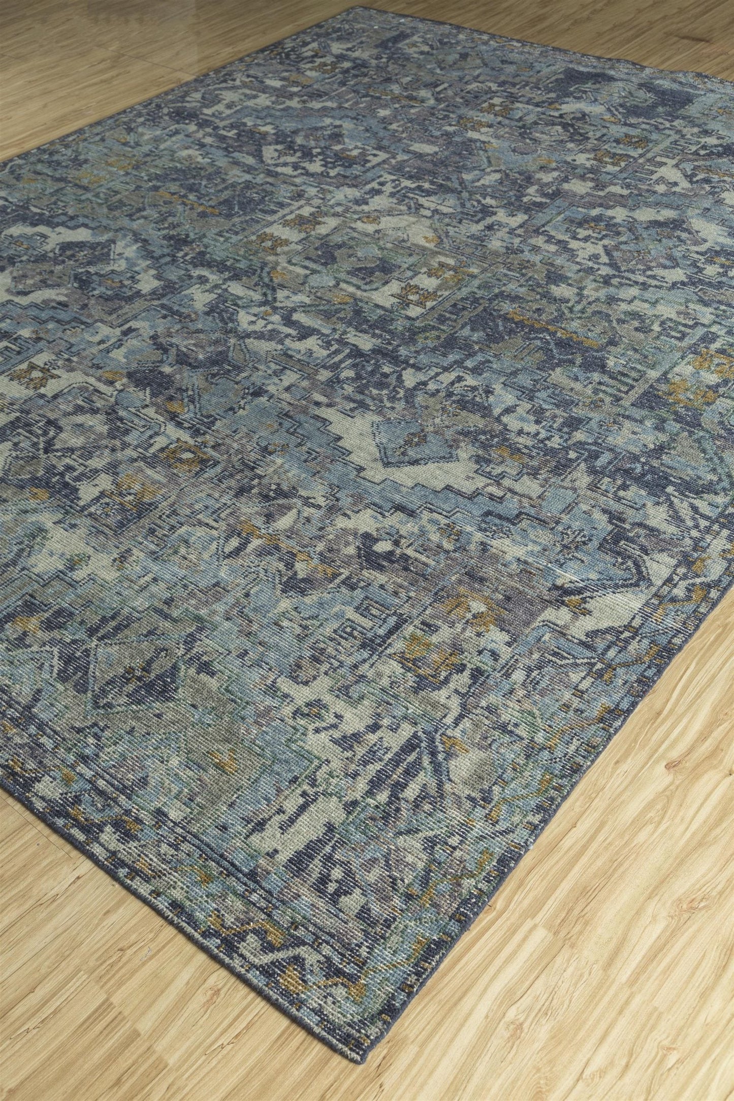 Handwoven rug with a transitional design, featuring blue, gray, and beige tones on a light wood floor.
