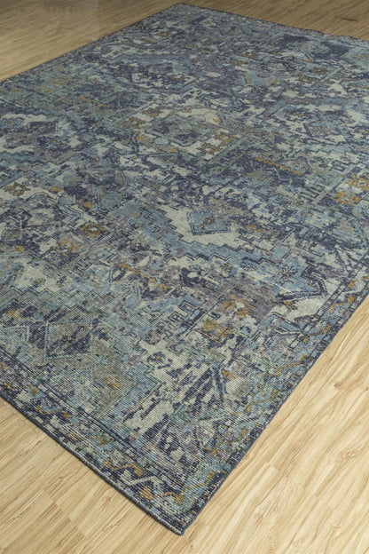 Handwoven rug with a transitional design, featuring blue, gray, and beige tones on a light wood floor.
