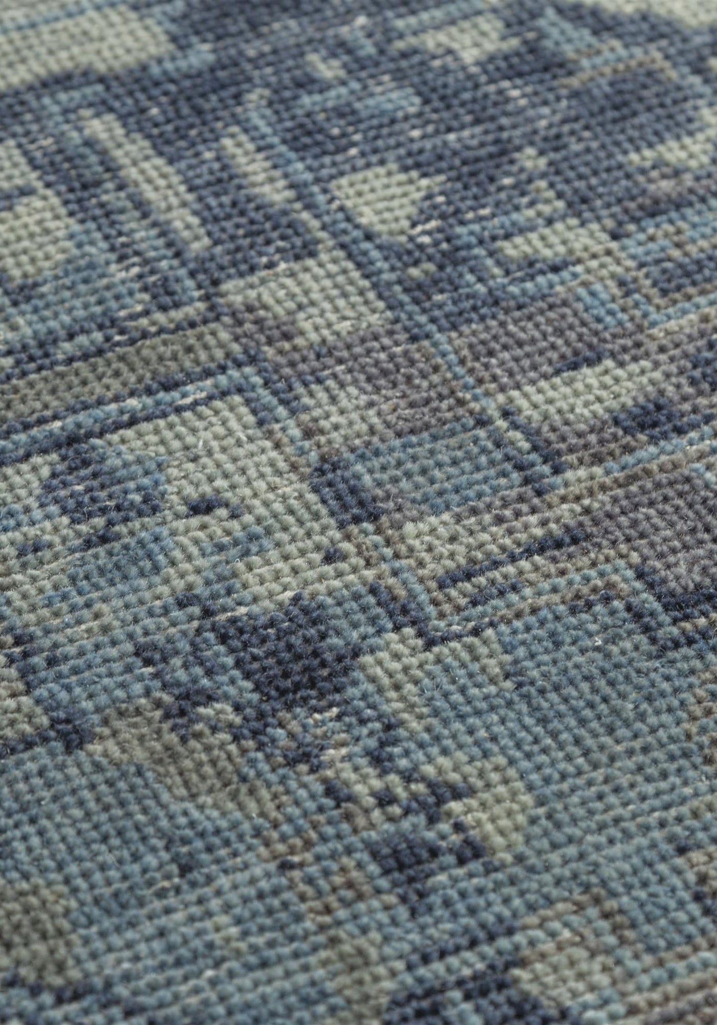 Close-up of handwoven rug texture, showcasing a muted blue and gray pattern.
