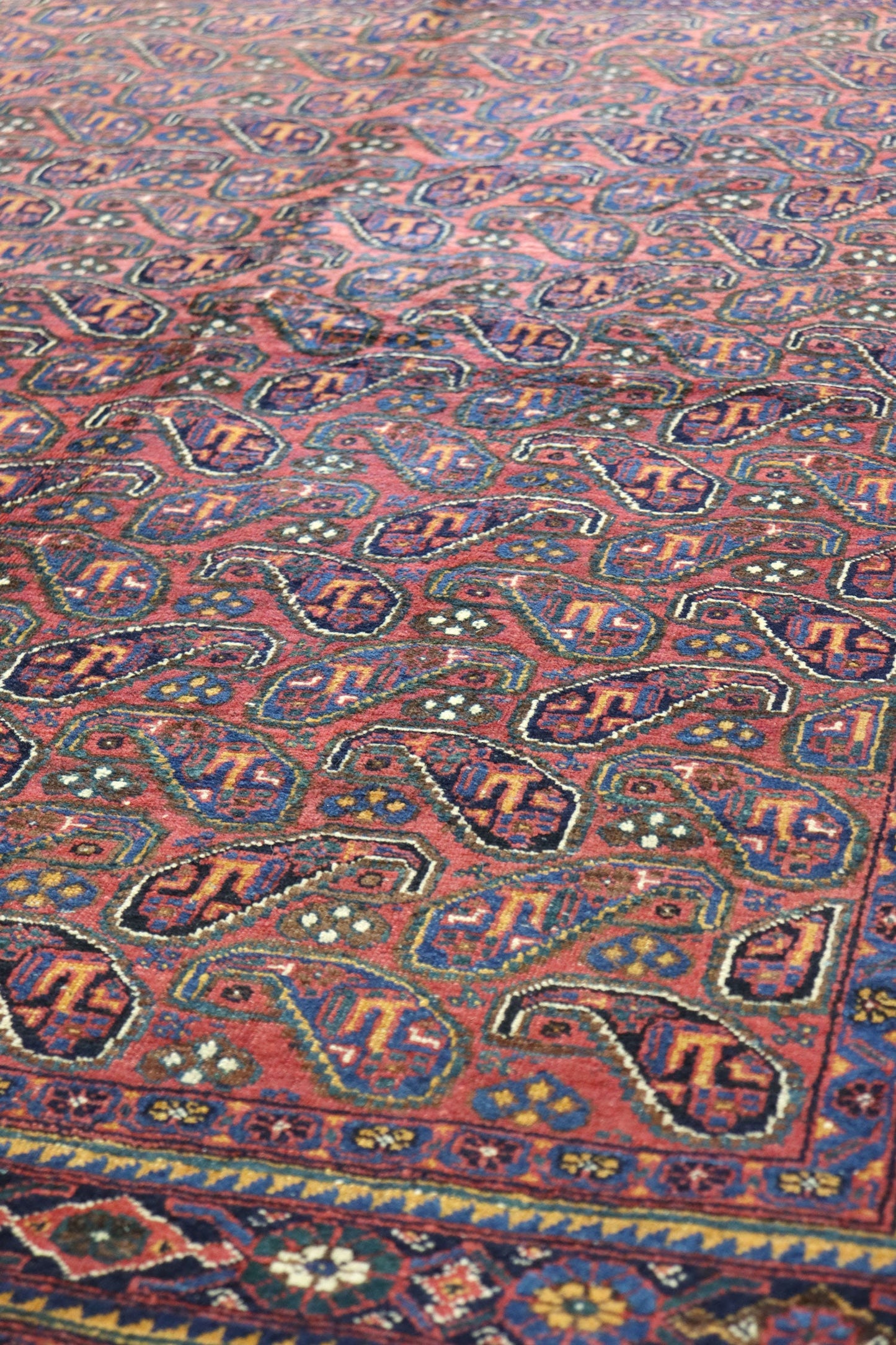 Detail of a handwoven tribal rug with a red base and intricate paisley pattern in blue, gold, and dark brown.
