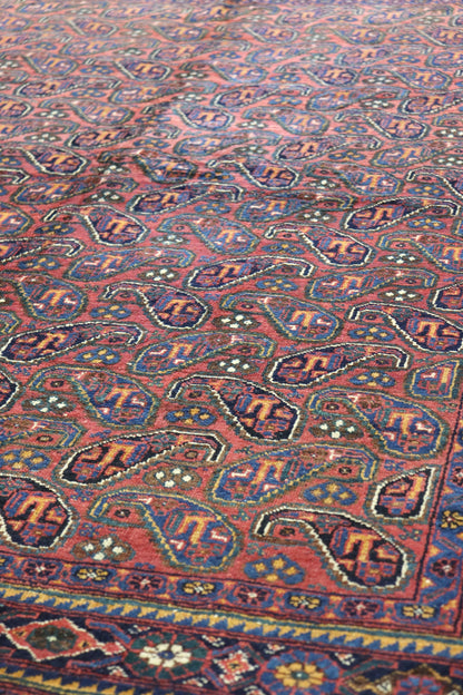 Detail of a handwoven tribal rug with a red base and intricate paisley pattern in blue, gold, and dark brown.
