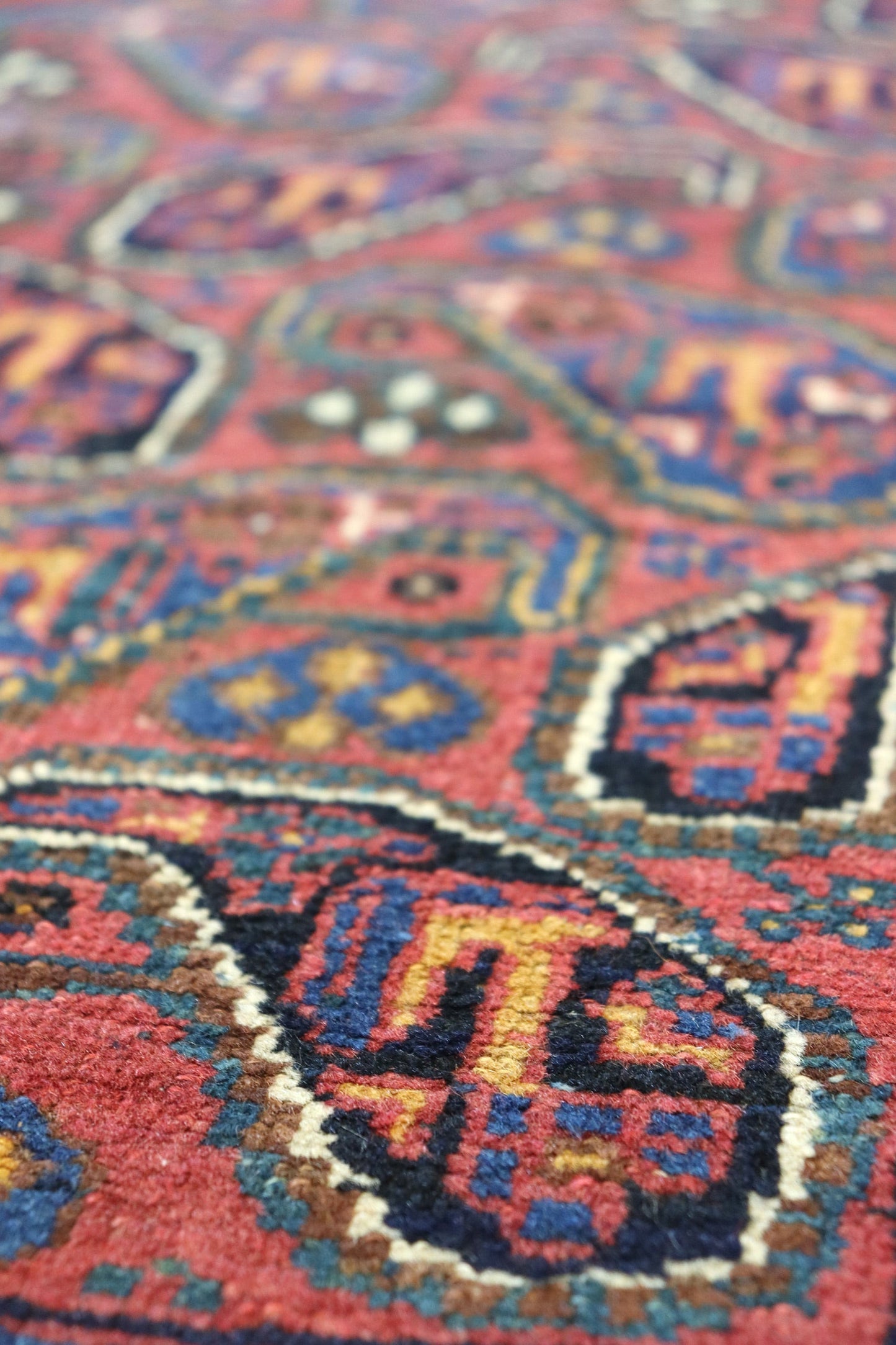 Close-up detail of a handwoven rug's intricate, red, blue, and gold pattern.
