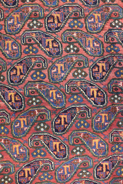 Close-up of antique Afshar rug's handwoven, red paisley pattern with blue, gold, and green details.
