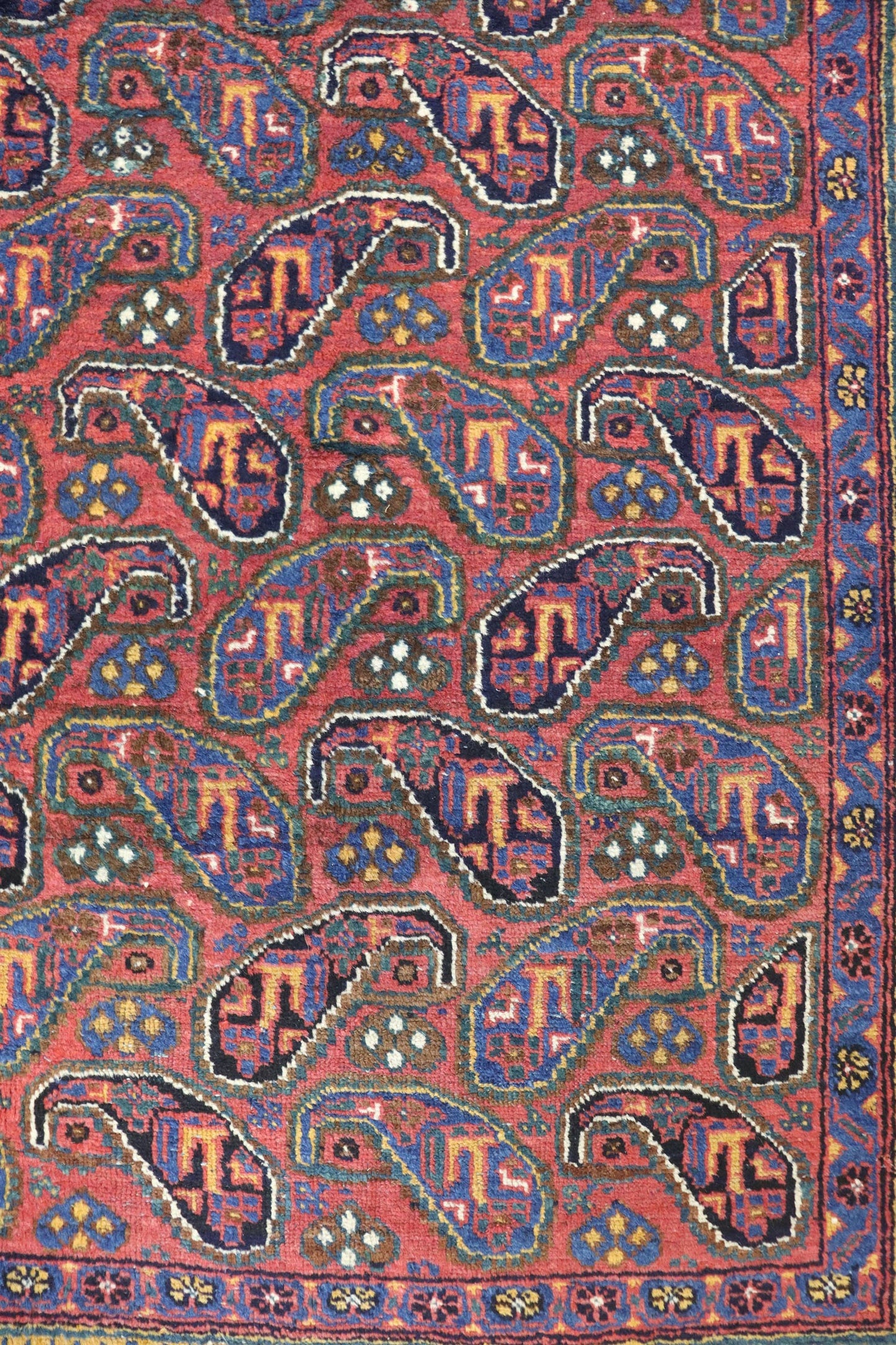 Handwoven tribal rug detail: red base with intricate paisley pattern in navy, teal, and gold.
