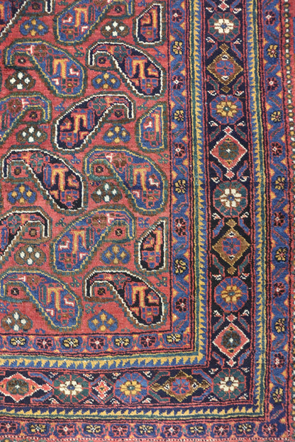 Handwoven tribal rug detail, showcasing a red base with intricate blue and gold paisley patterns and a richly colored border.
