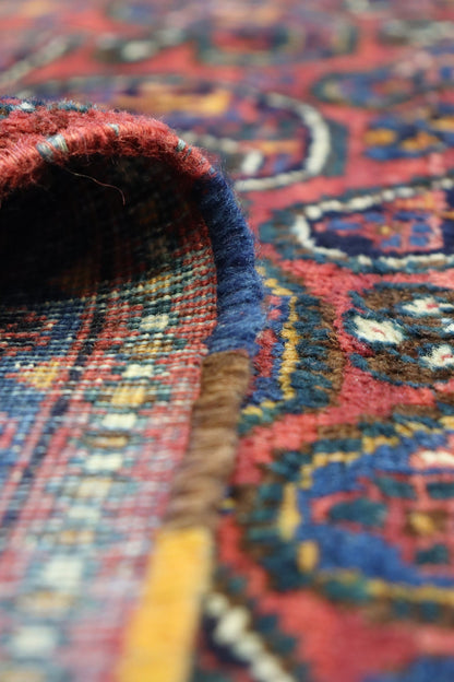 Close-up of handwoven rug's detailed texture, showcasing rich reds, blues, and golds in intricate tribal pattern.
