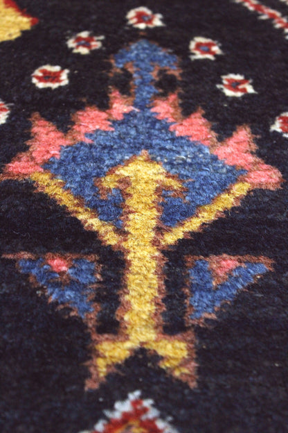 Close-up detail of a dark rug's handwoven floral pattern in blue, red, and gold.
