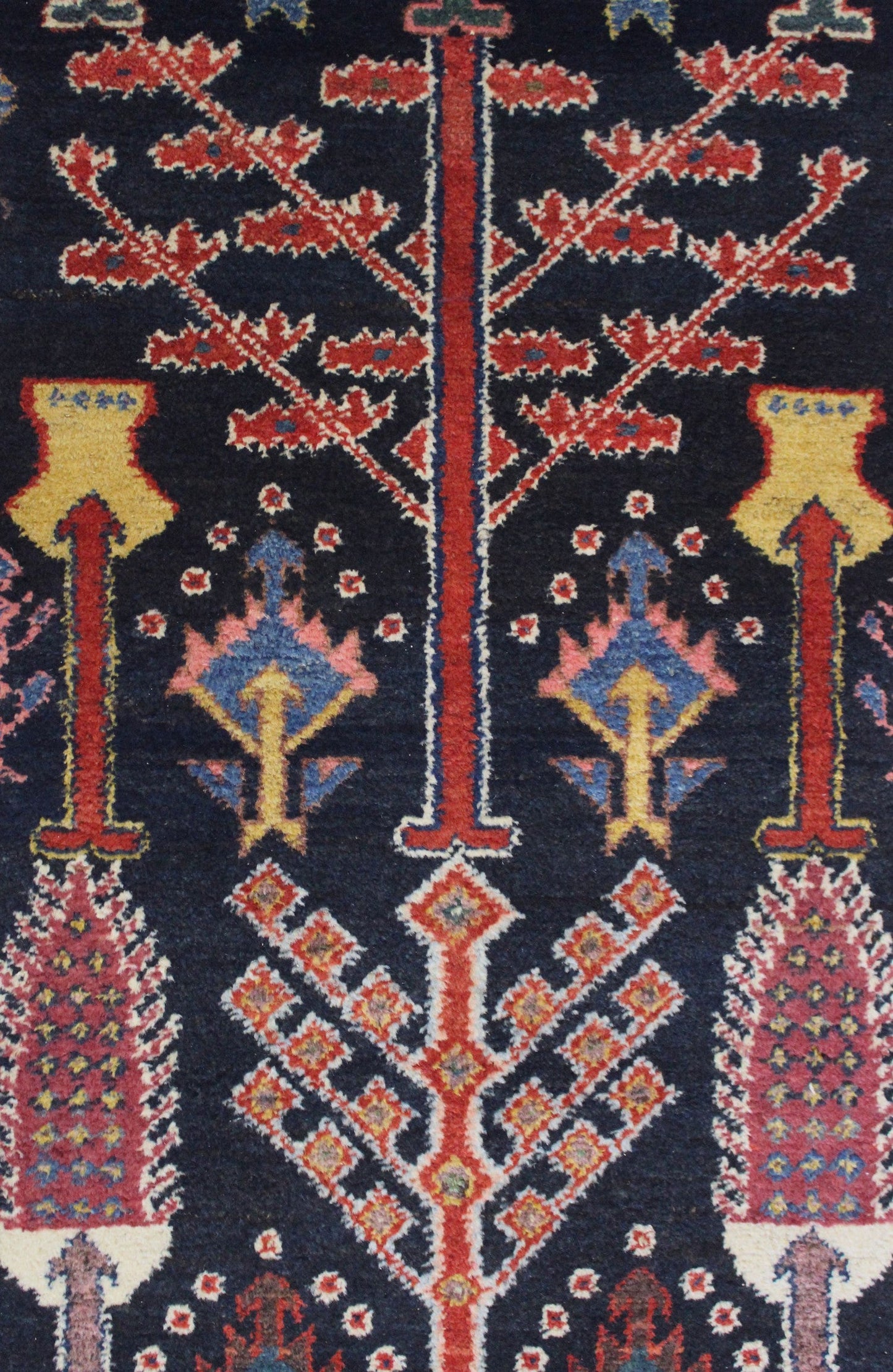 Close-up detail of a dark-navy antique rug with intricate red, pink, and gold floral patterns.
