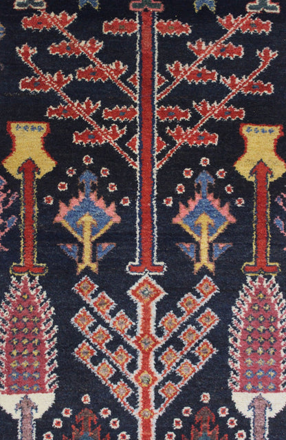Close-up detail of a dark-navy antique rug with intricate red, pink, and gold floral patterns.
