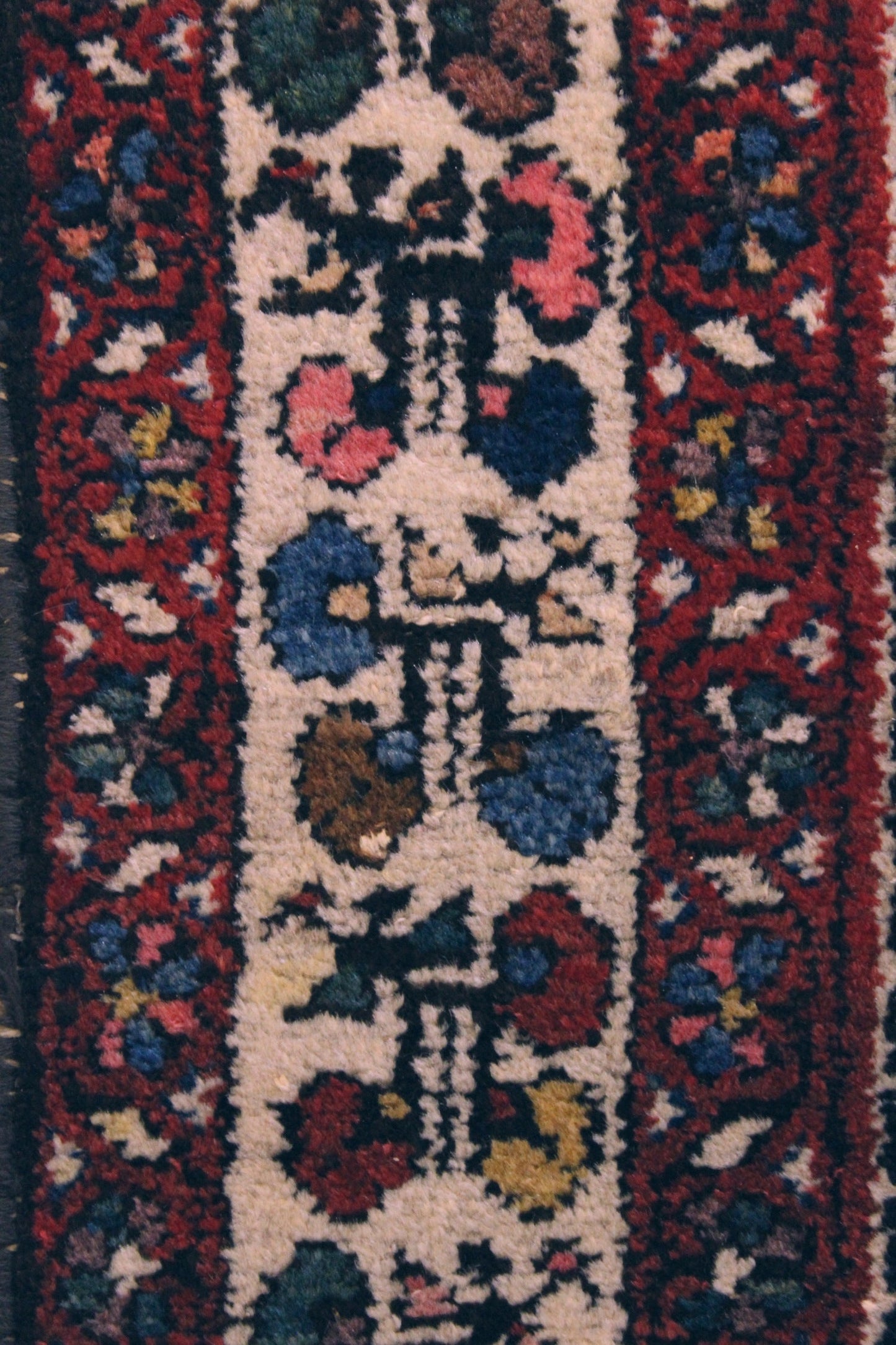 Close-up of antique rug detail: handwoven, multicolored floral pattern on a cream background.
