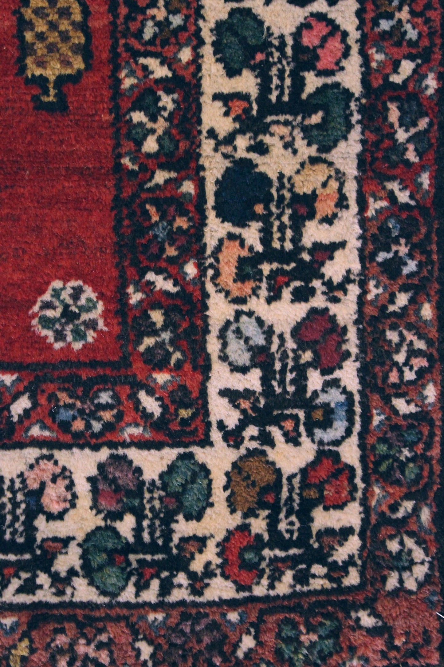 Close-up of antique rug's detailed border, showcasing handwoven floral pattern in red, cream, and dark hues.
